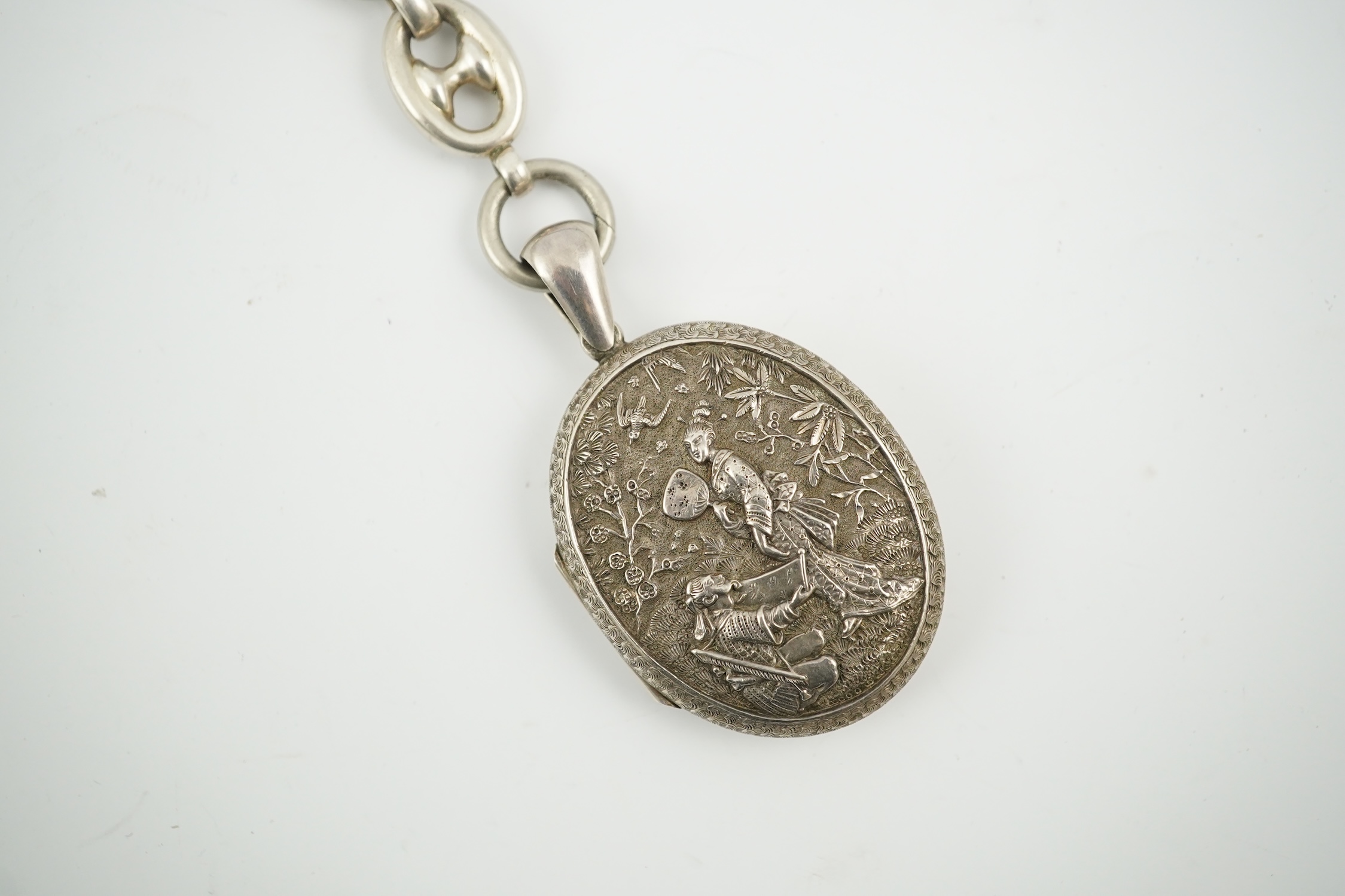 A late Victorian white metal oval locket with Japonaiserie decoration, 47mm, on a white metal chain. Condition - fair to good